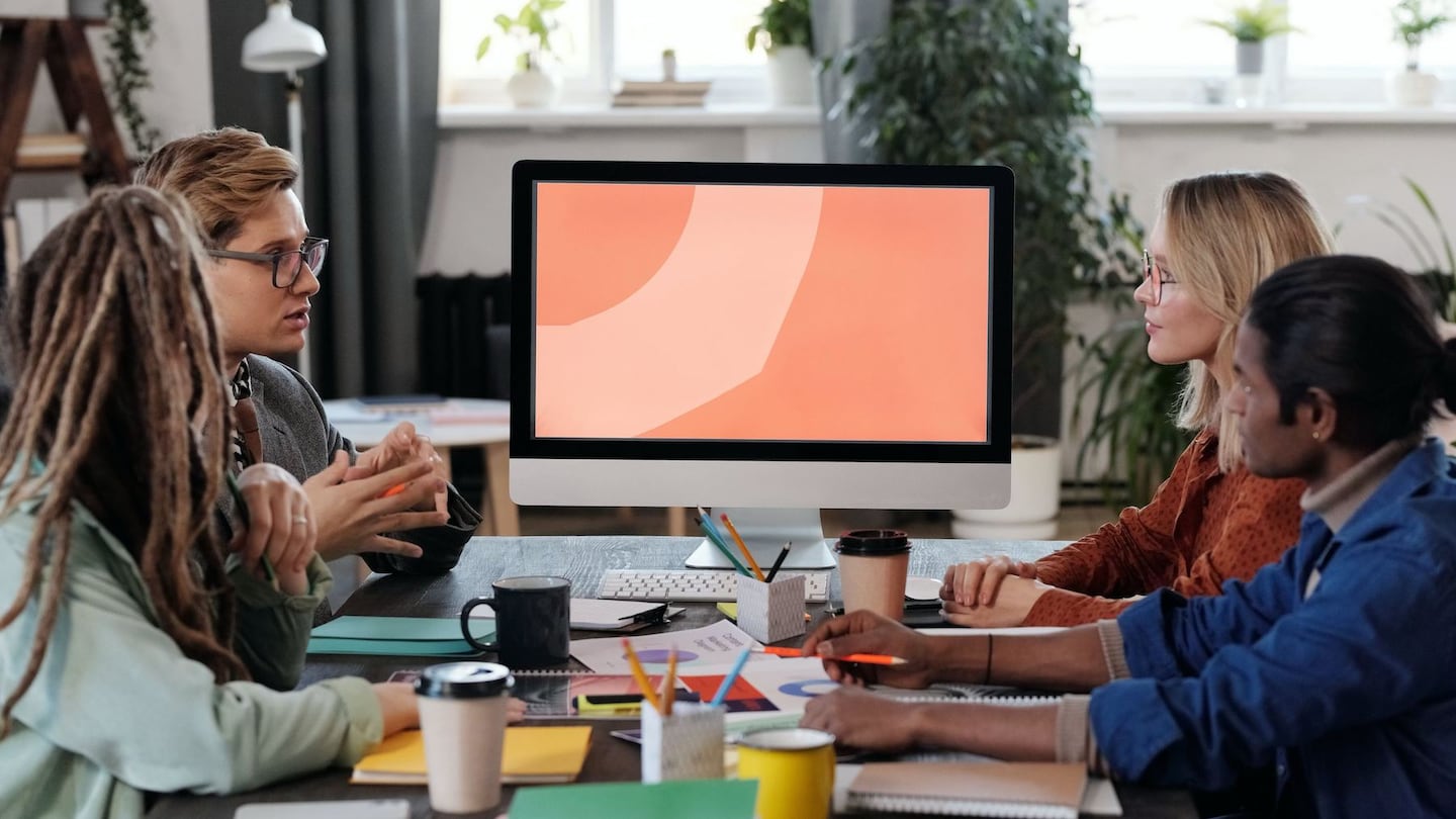 A group of four employees having a discussion while sitting at a desk.