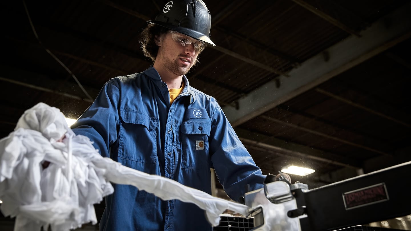 A man in work overalls and a hard hat feeds material into a machine for recycling.